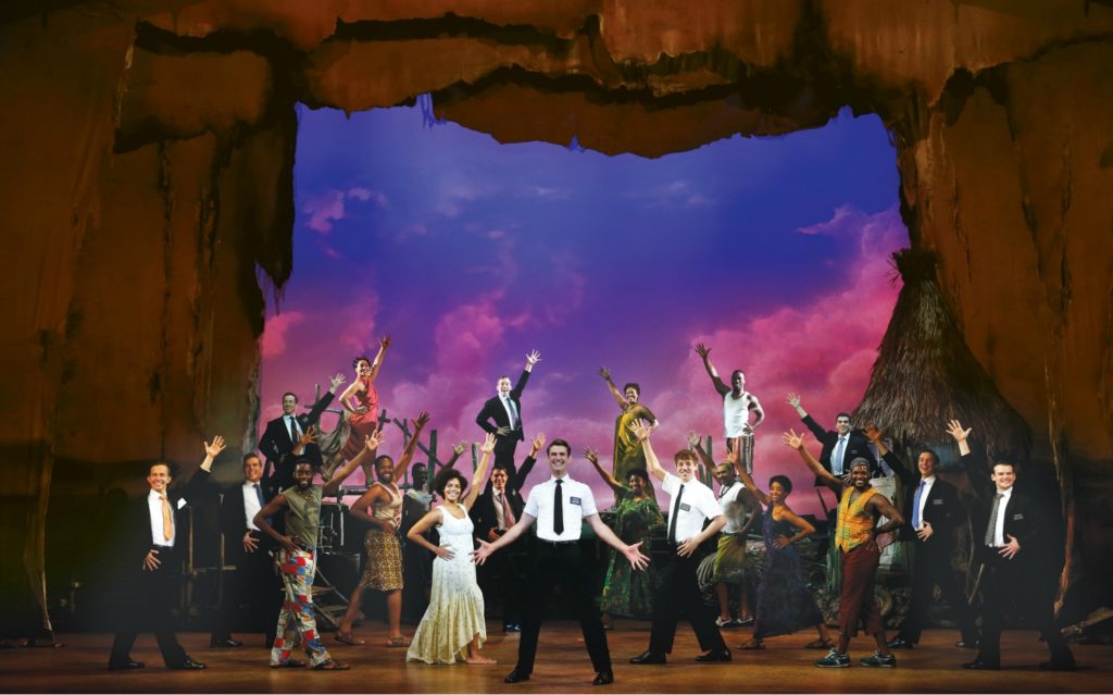 Ryan Bondy, centre, as Elder Price, Zahra Newman, left, as Nabulungi, A.J. Holmes, right, as Elder Cunningham, and company in the Australian premiere of THE BOOK OF MORMON at the Princess Theatre, Melbourne. © Jeff Busby